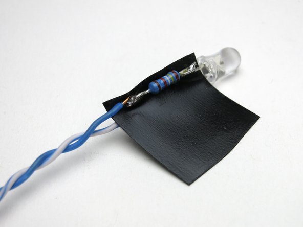 Add the resistor in line with either side, it doesn't matter which. In this photo it's on the cathode, indicated by the physical structure inside the lens being bigger, and the part that lights up.