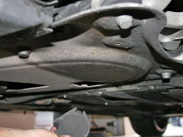 Remove the small round plastic cover that hides the oil drain plug, under the car. You’ll find this located in the middle of the aluminum under panel, close to the front center jack point.