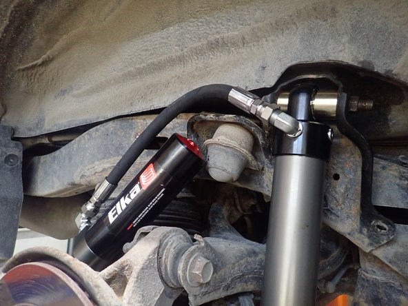 With the reservoir hose facing the rear of vehicle, compress shock then install upper bolt. (Right side shown)