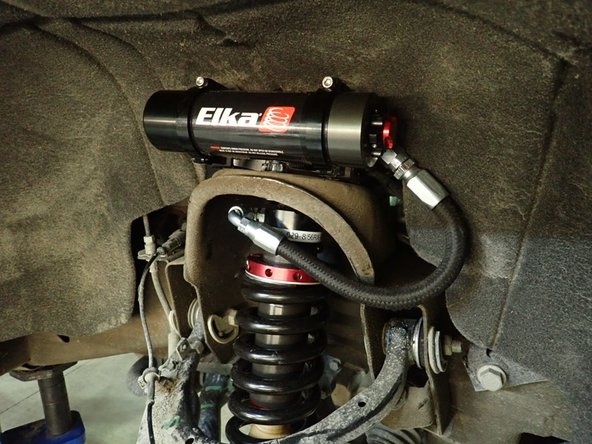 Sit reservoir into bracket's clamps, then place the reservoir in a way to place reservoir fitting and hoses as close to the fender guard as possible. BE CAREFUL TO NOT OVERBEND THE HOSE OR MAKE THE HOSE RUBBING ON UPPER SHOCK MOUNT IN THE AREA SHOWED BY RED CIRCLE.