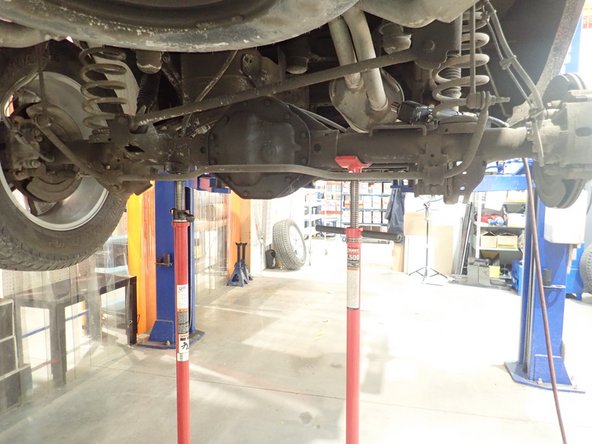Using an underhoist stand or a jack, lift slightly rear axle to be able to remove lower bolt.