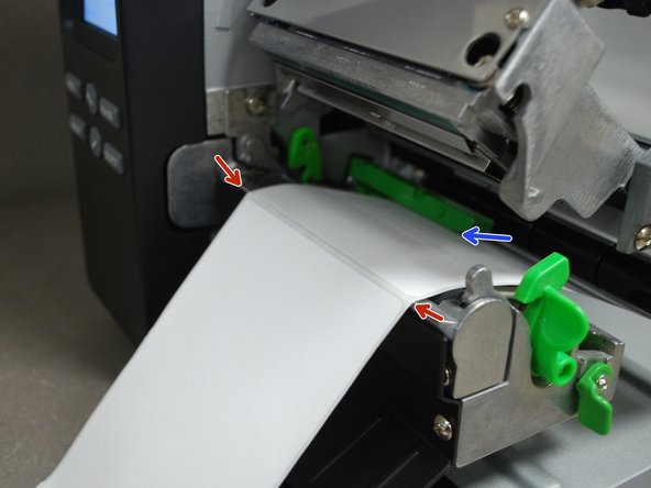 Pull through until the leading edge of one label is even with the tear-off edge (red arrows).