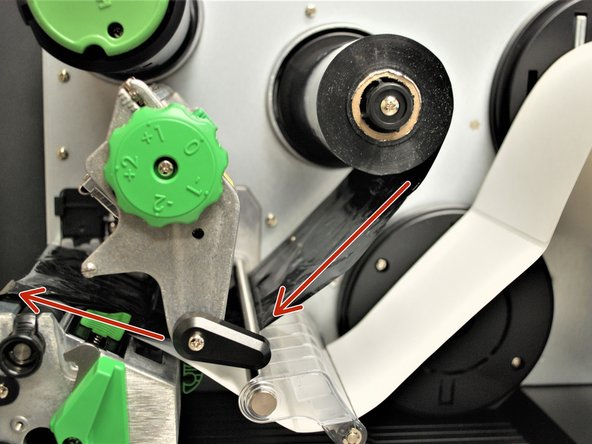 Feed the ribbon under the printhead and out to the front, making sure to feed it above the media sensor (the black clip on the bottom of the printhead, shown by the blue box).