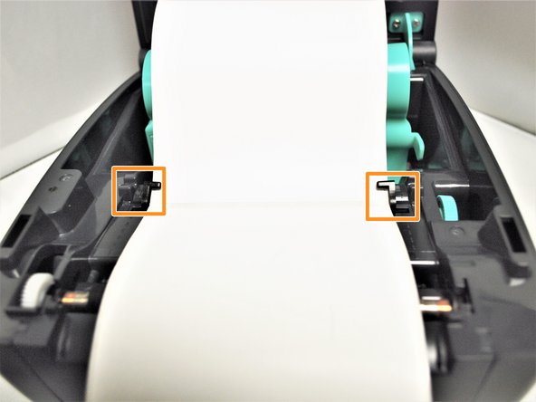 While pressing the labels flush, spin the green Media Guide Adjustment Knob on the right, shown by the blue arrows in Image 2, towards the front of the printer.