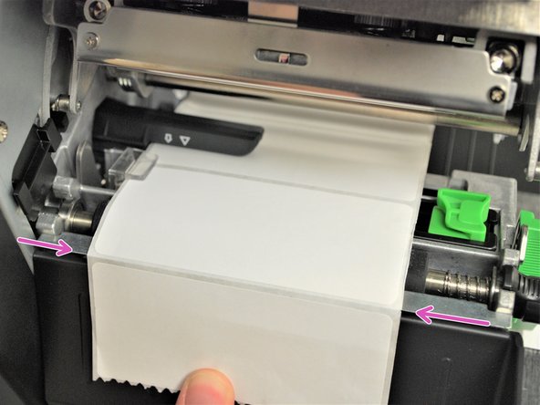 Pull through until the leading edge of one label is even with the perforated  tear-off edge (pink arrows).