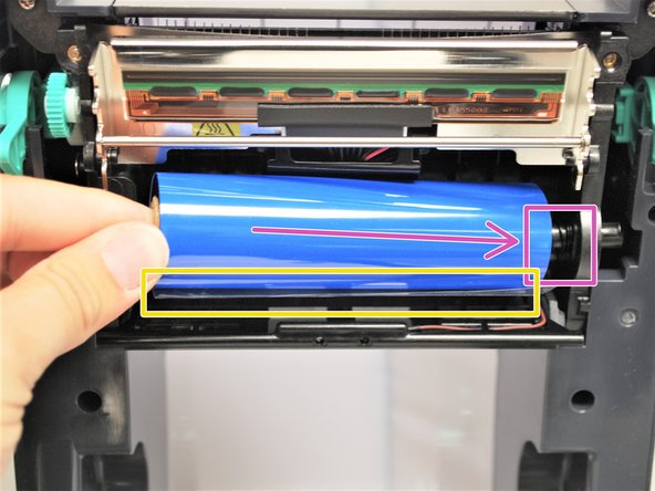 Insert the ribbon by first pressing it into the spring loaded holder on the right.