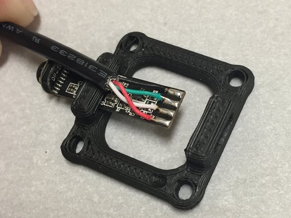 Solder the wires to the pads, as shown.  Make sure that you're doing this while the camera is placed half-way into the PLA piece.  The wires should go out towards the camera lens.