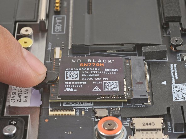 Use your finger to press down on the black SSD latch to unlatch the SSD.