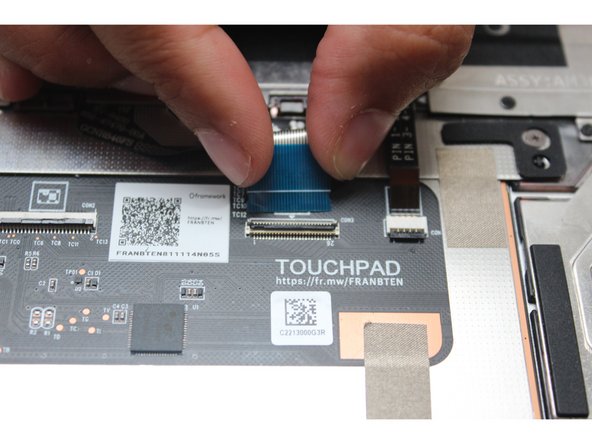 Using the spudger end of the Framework Screwdriver or your fingernail, disconnect the Keyboard Membrane from the Touchpad Module by switching the black latch up and sliding the cable straight out.