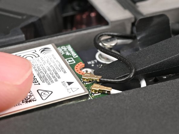 While holding the Wi-Fi module down, insert the flat end of your Framework Screwdriver under one of the coaxial connectors, where the cable meets the metal head.