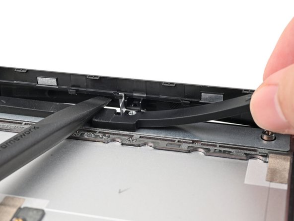 While keeping the plastic strip bent, lift the rubber spacer out of its screw posts and remove it.