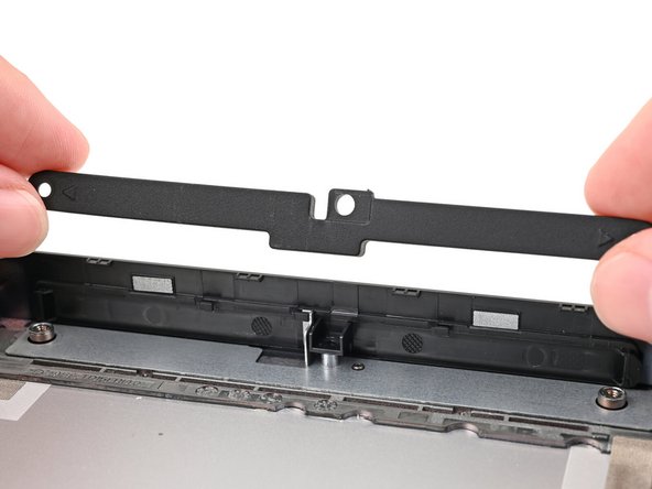 While keeping the plastic strip bent, lift the rubber spacer out of its screw posts and remove it.