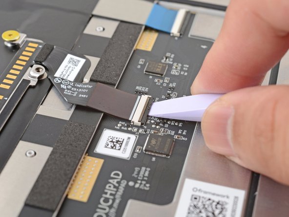 Use the flat end of your Framework Screwdriver or a fingernail to gently pry up the black locking tab on the touchpad cable ZIF connector, located on the back of the touchpad.