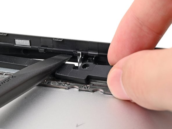 While keeping the plastic strip bent, lift the rubber spacer out of its screw posts and remove it.