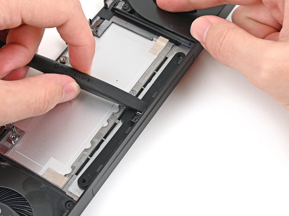 While holding the Expansion Bay Shell down, use the flat end of your Framework Screwdriver to push the plastic strip near the rubber spacer outwards.