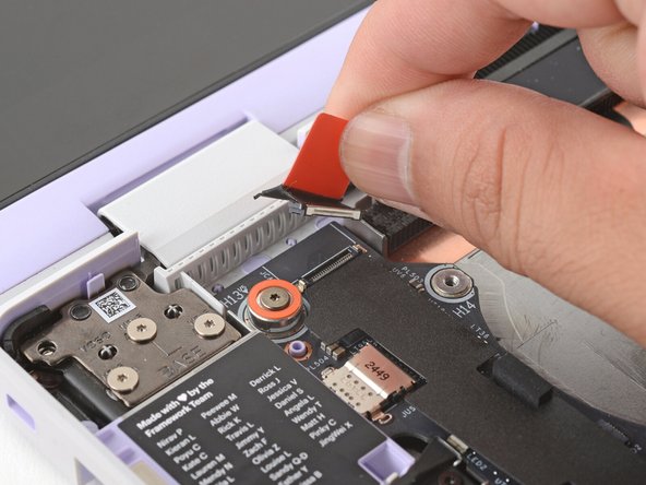 Use your fingers to grab the orange tab on the webcam cable, located near the left hinge.