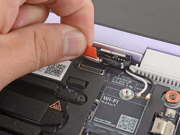 Use your fingers to grab the orange tab on the display cable, located near the right hinge.