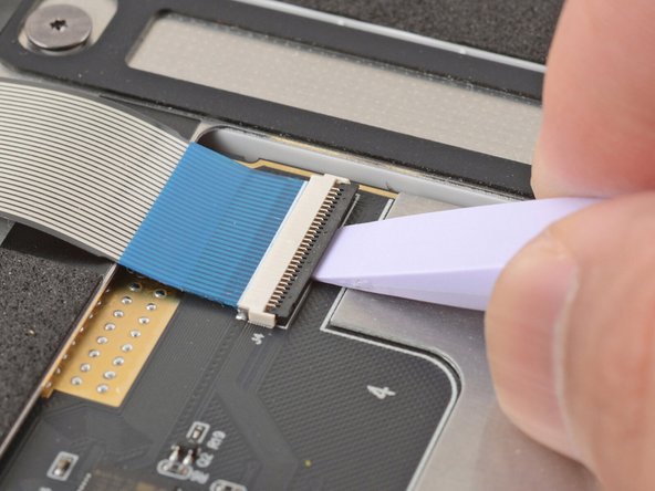 Use the flat end of your Framework Screwdriver or a fingernail to gently pry up the black locking tab on the keyboard cable ZIF connector, located on the back of the touchpad.