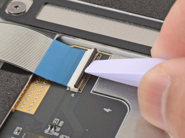 Use the flat end of your Framework Screwdriver or a fingernail to gently pry up the black locking tab on the keyboard cable ZIF connector, located on the back of the touchpad.
