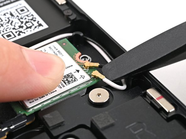 While holding the Wi-Fi module down, insert the flat end of your Framework Screwdriver under one of the coaxial connectors, where the cable meets the metal head.