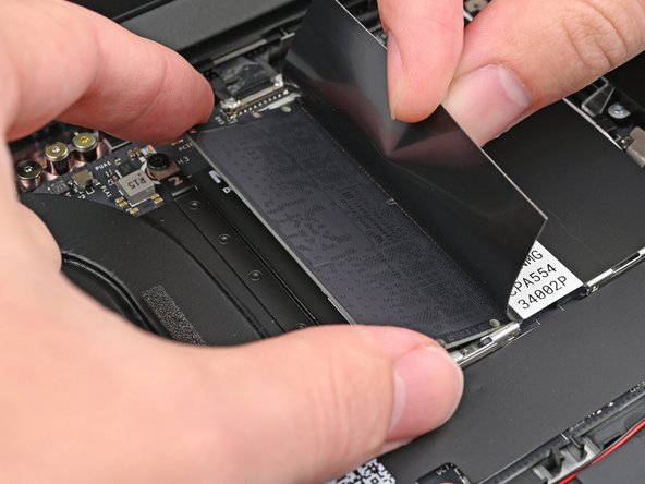 While holding up the black flap covering the left memory module, push the two metal arms on each side of the module outward until they disengage and the module pops up at a shallow angle.