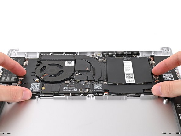 Grab the Mainboard by its edges and place it into the Bottom Cover and onto its alignment pegs.