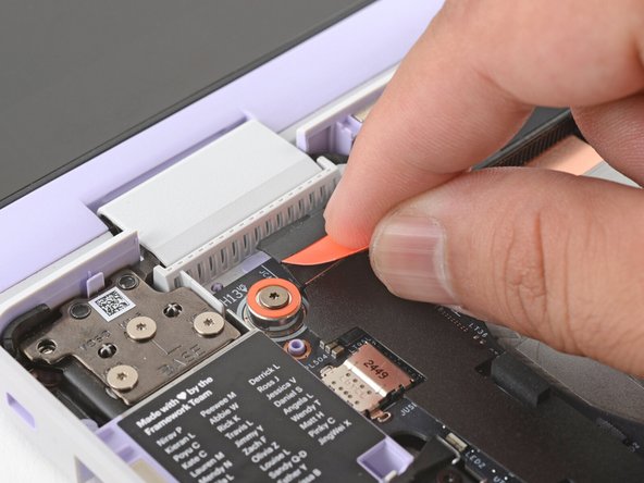 Use your fingers to grab the orange tab on the webcam cable, located near the left hinge.