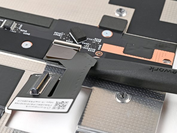 Slide the flat end of the Framework Screwdriver under the Mid Plate Cable, near the ZIF connector, to separate the adhesive.