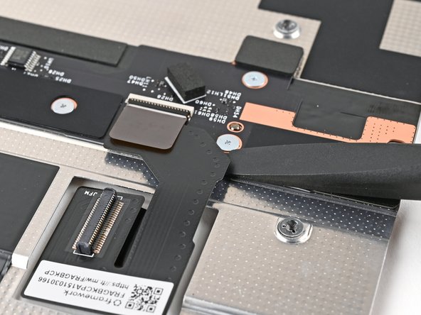 Slide the flat end of the Framework Screwdriver under the Mid Plate Cable, near the ZIF connector, to separate the adhesive.