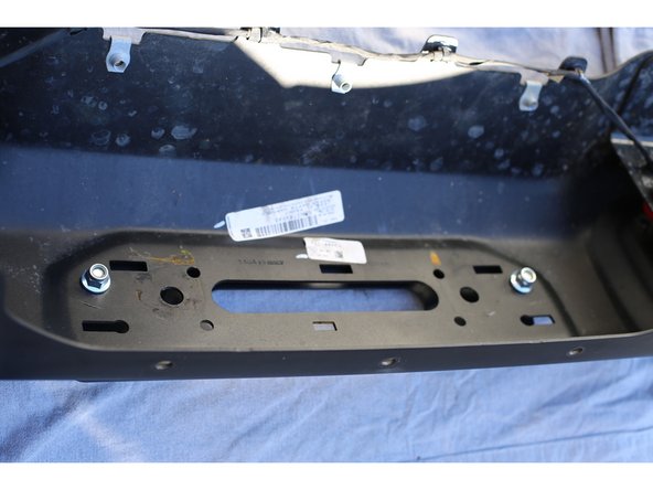 Using a flat blade screwdriver, remove the plastic blanking plate or license plate mount from the front of the bumper by freeing the 6 clips.