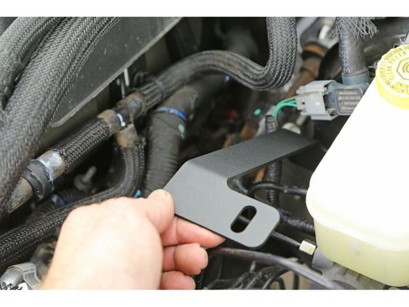 Install the compressor mount gusset onto the stud behind the nut you just loosened. The closed slotted hole should be facing up (as shown). The open slot should slide down between the nut and the master cylinder.