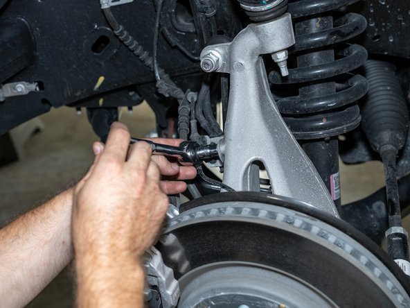 Using a 10mm socket/wrench, remove the brake line/ABS bracket from the knuckle.