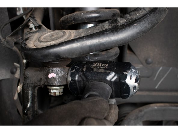 Strike the spindle with a large hammer where the upper ball joint stud engages the spindle. A couple quick strikes should separate the taper. Alternatively, a ball joint separator may be used.