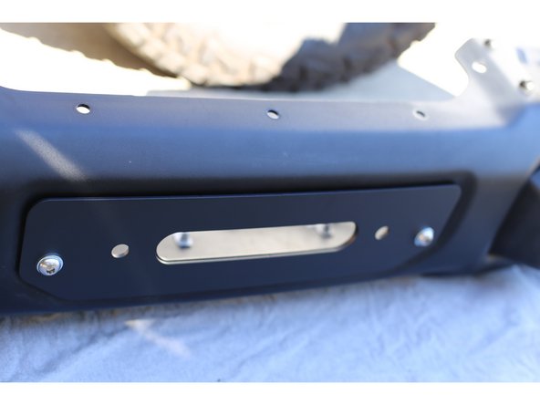 Using the two provided M10-1.50 x 40mm stainless steel button head bolts with a washer under each bolt head, attach the Grimm OffRoad Fairlead Mounting Plate to the bumper in place of the factory blanking plate. Place the bolts in the outer holes.