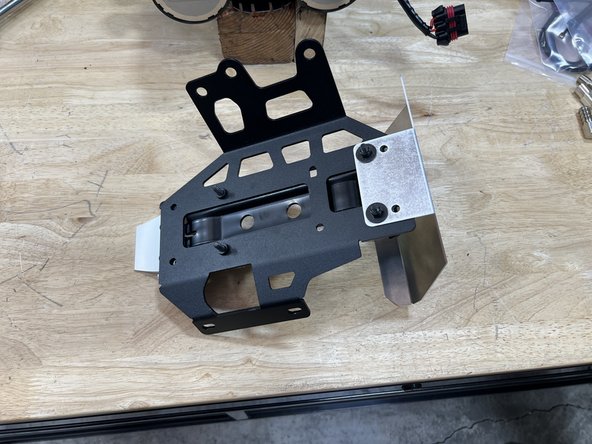 With the compressor oriented as shown with the compressor mounting holes facing up, the ARB mounting bracket should be positioned with the cam-clamp on the left. Orient the Grimm OffRoad Compressor Bracket and heat shield into the Compressor as shown.