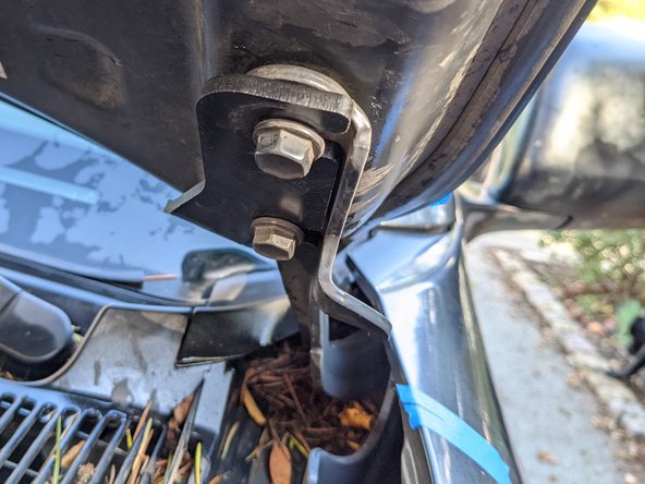 With the mounts loose, feed the bracket with light from the windshield side carefully under the open hood, and slide the bracket in between the bolt heads and the hinge. You may have to squeeze the hood to the hinge with one hand while sliding the bracket in with the other hand.
