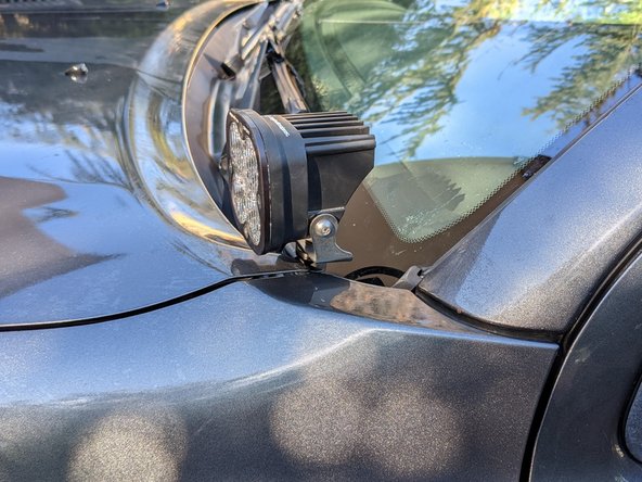 Loosen the hood hinge bolts, place the light bracket on, and then snug the bolts.