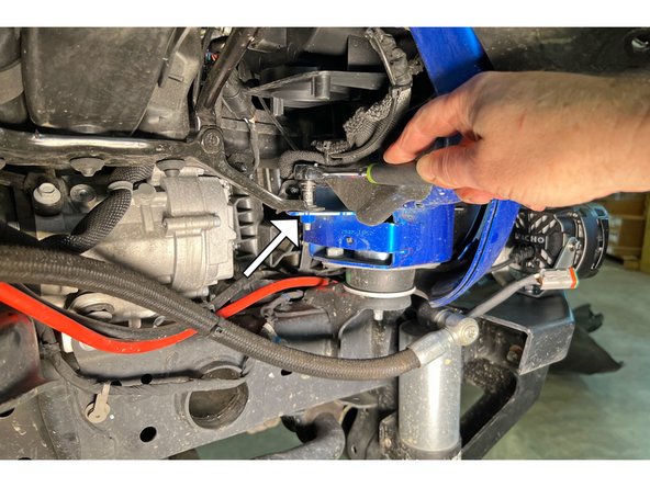 Using a 10mm socket/wrench, remove the screw behind the front body mount as shown.