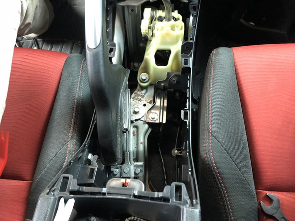 Open the center console storage compartment and use a plastic trim tool to pop the cup-holder section up. Start on the edges and pull upwards while prying. It will pop loose and expose the shifter and e-brake assembly.