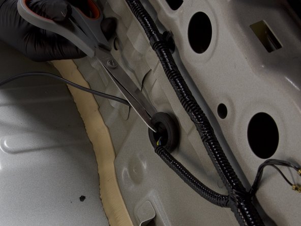 Use a pair of scissors or knife and cut a slit into the factory grommet. Feed the wire through the slit and re-install the grommet in place.