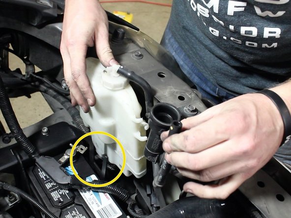 Slide the overflow tank onto the upper battery bracket.