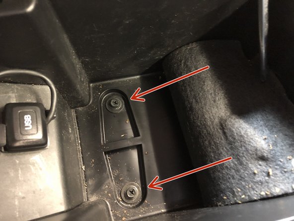 Inside of the console compartment, lift up the lower covering an expose the two Phillips head screws. Remove them.