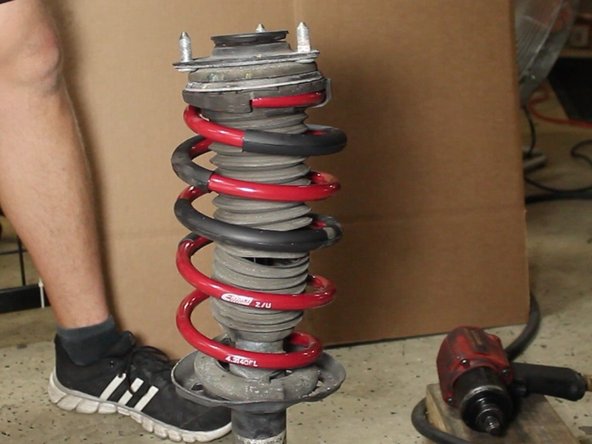 The new spring is shorter than the factory spring, this should allow you to slightly press down on the spring to get the threaded section of the strut to come through the top hat. If not, please use the spring compressors.