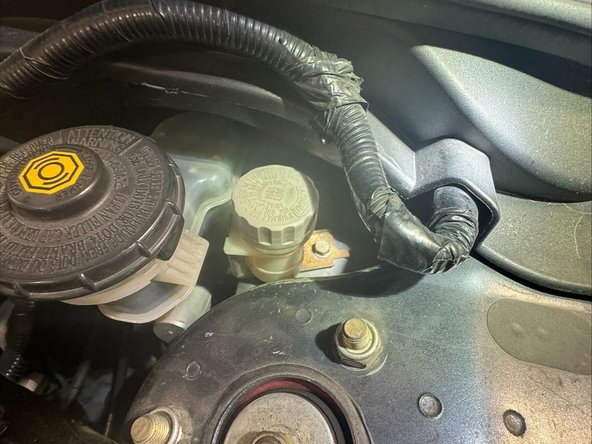 Remove the x1 M6x1.0 bolt mounting reservoir to strut tower. Use a 10mm socket and extension.