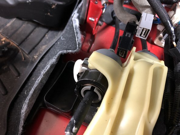 On the LH cable, push the white tab upwards to unlock the shifter cable.