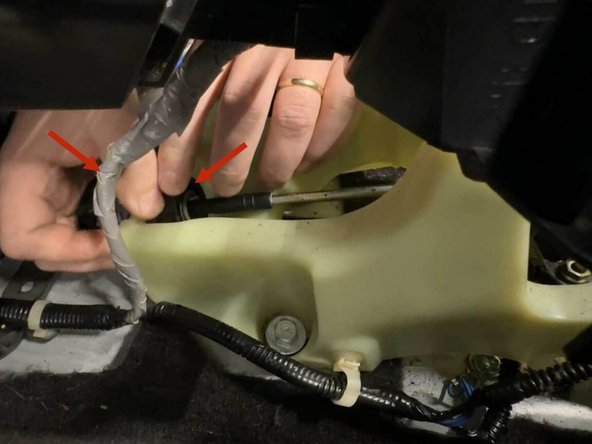 The shifter cable is secured to the shifter by a twist-lock collar. Pull the white locking tab straight out, then rotate the black collar counter-clockwise until the internal spring bottoms out (it’s stiff, so expect a few firm turns). Once the collar stops, slide the cable housing straight up out of the shifter plastic.