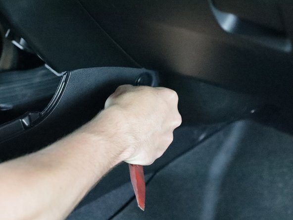 Use a trim tool and remove the three retaining clips from the front corners of the console.