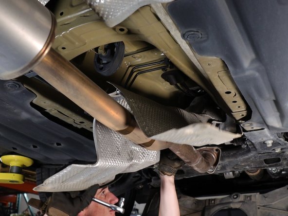 Unbolt and remove the lower heat shield. This will expose the shifter cables.