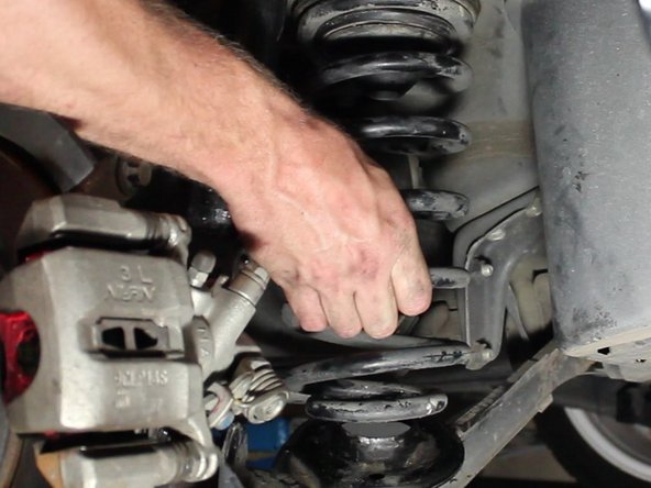 Press down on the brake rotor to push down the lower control arm. This will depress the spring and allow it to be removed.