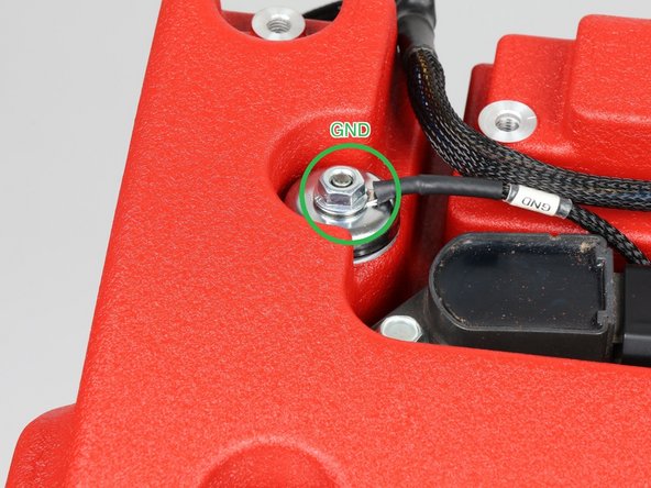 Land the ground eyelet (labeled GND, green ring) on the valve cover stud. The stud must be clean bare metal and the nut tightened down. A loose or painted-over ground causes strange problems that are hard to chase.